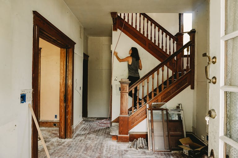 A woman working on home renovation featuring a wooden staircase.