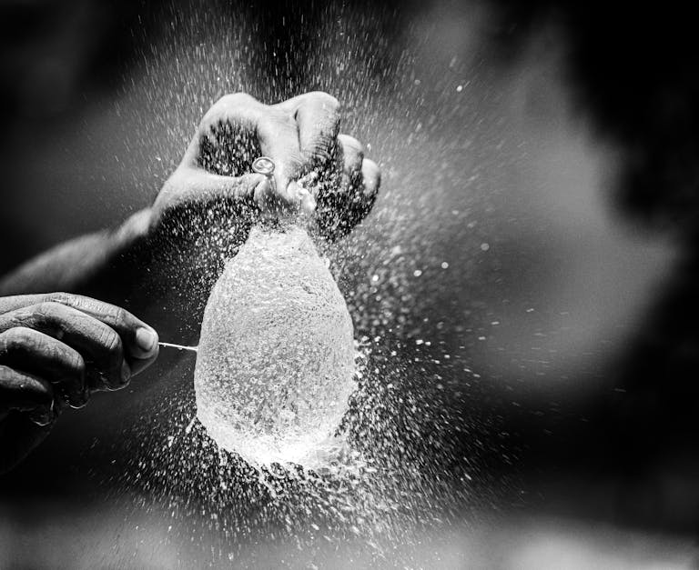Captivating moment of a water balloon explosion captured in monochrome, showcasing motion and texture.